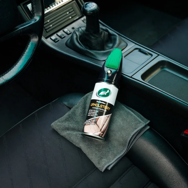 Een Turtle Wax-bekledingsreiniger met applicatorborstel in een auto-interieur.